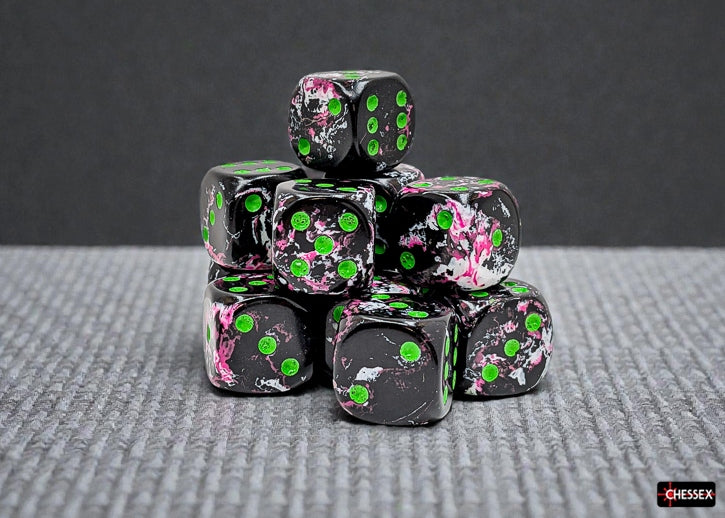 Stack of black dice with white, pink, and green brush patterns and green pips on a gray surface