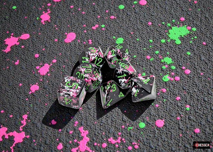 Set of Chessex dice with pink and green ink splashes on a dark surface